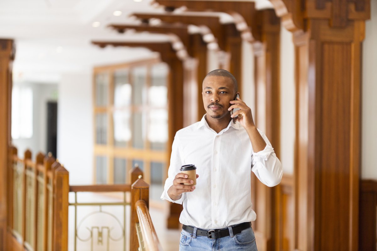 Black business man at work holding coffee and talking on the phone