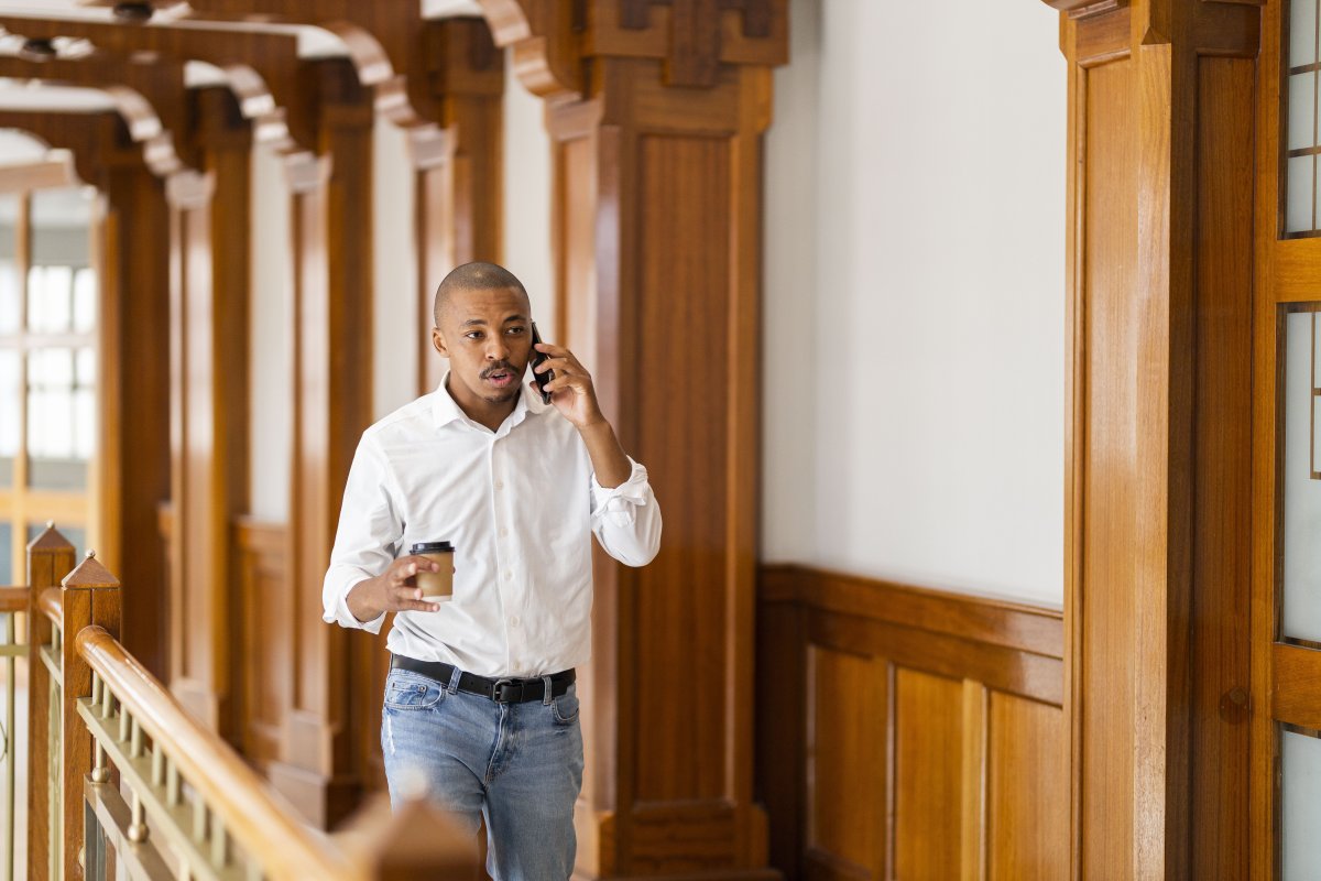 Black business man at work holding coffee and talking on the phone