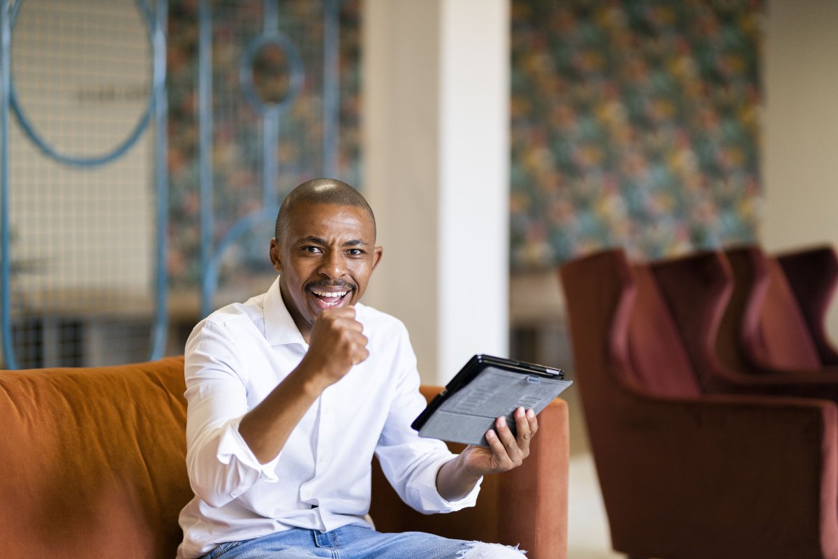 Black business man celebrating a win with a fist pump and looking at his tablet