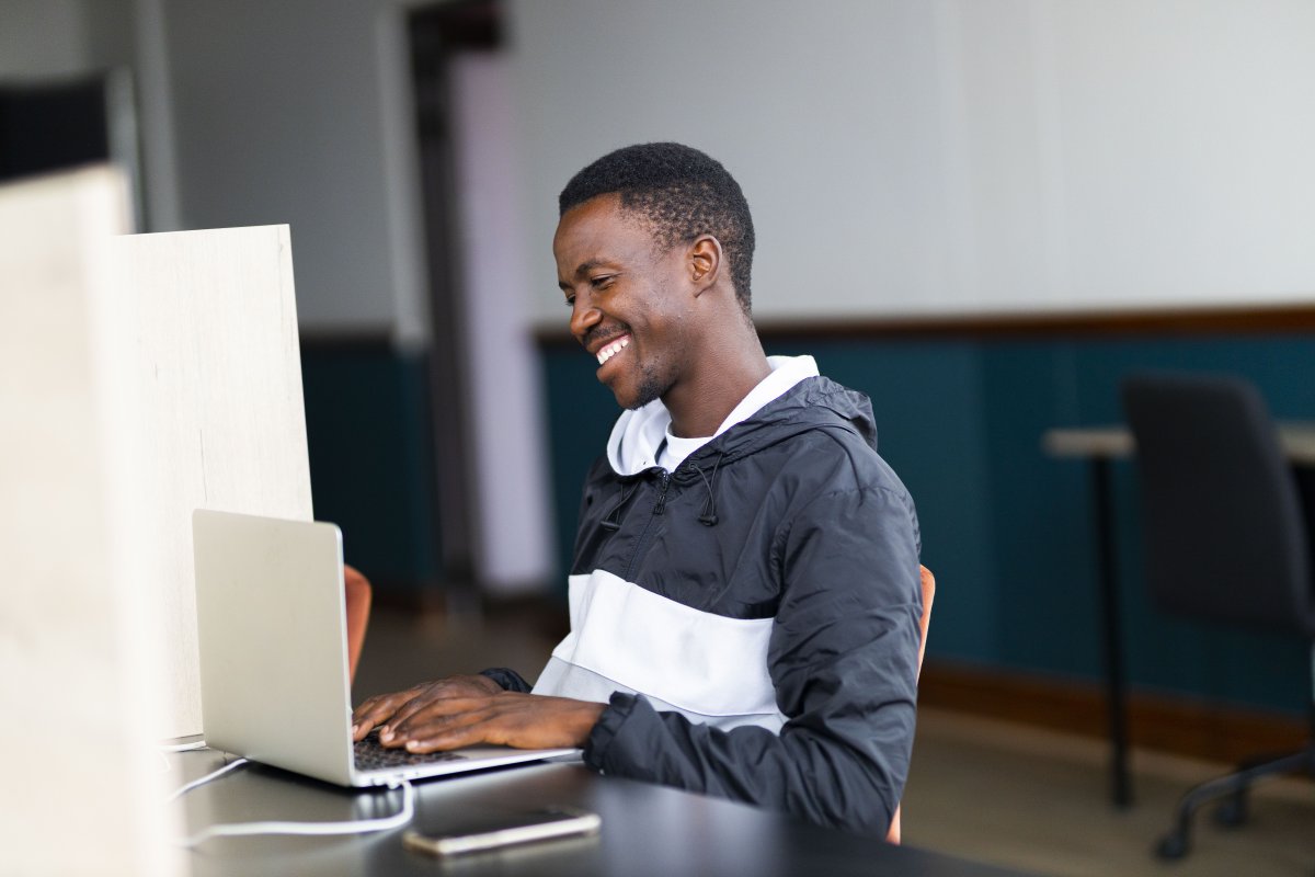 Black man celebrating looking at his laptop with a grin