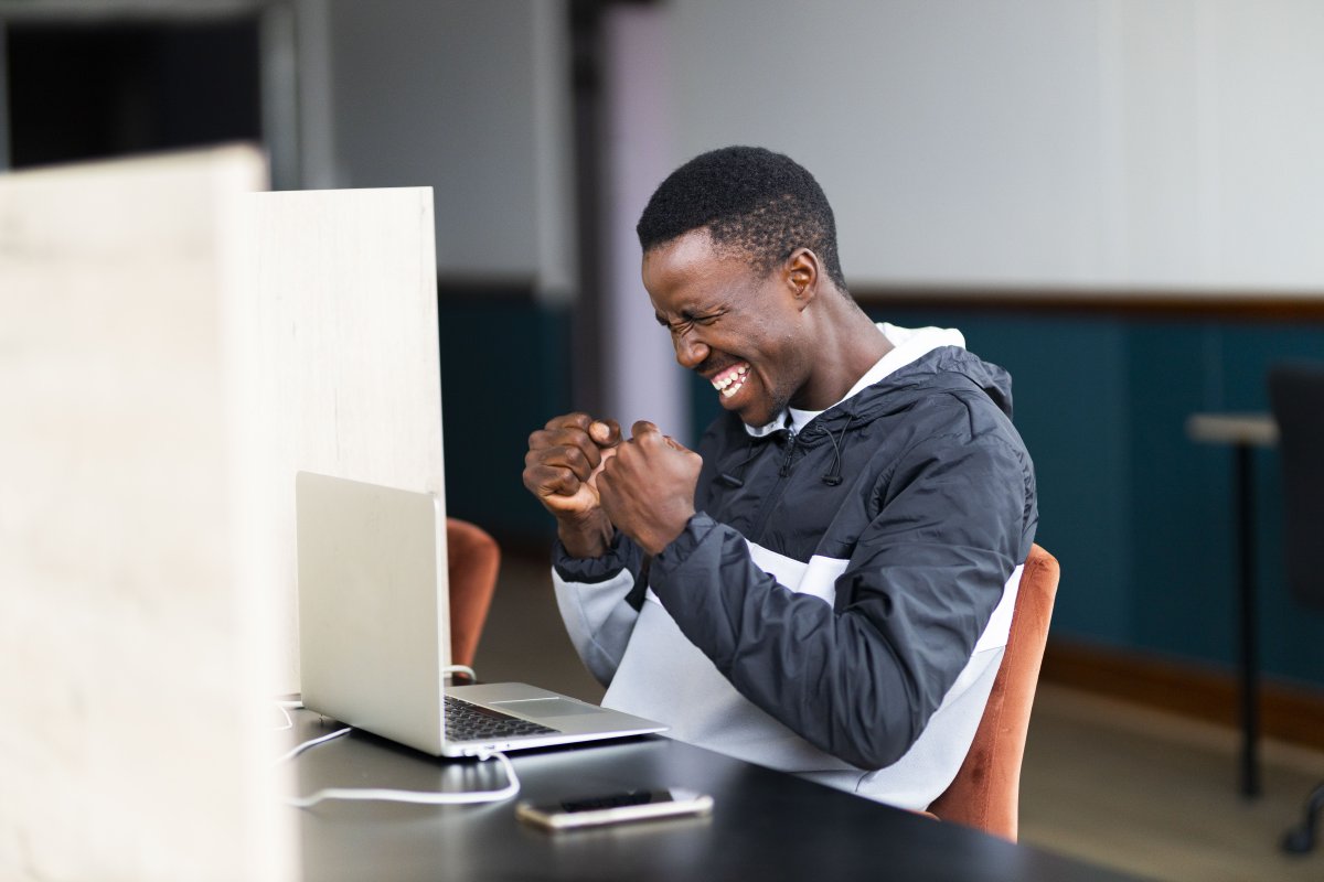 Black man celebrating a win and looking at his laptop