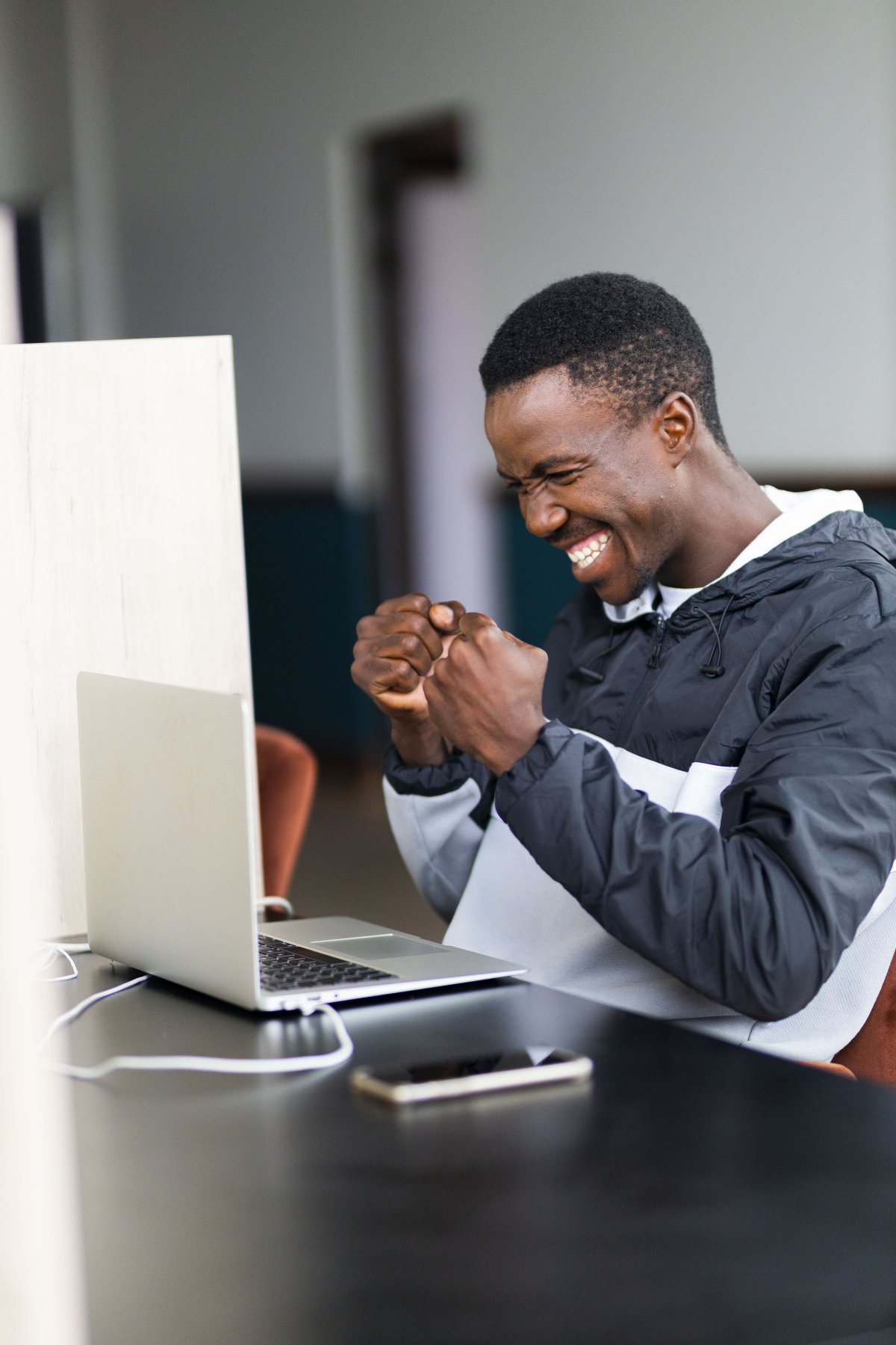 Black man celebrating a win and looking at his laptop with a grin