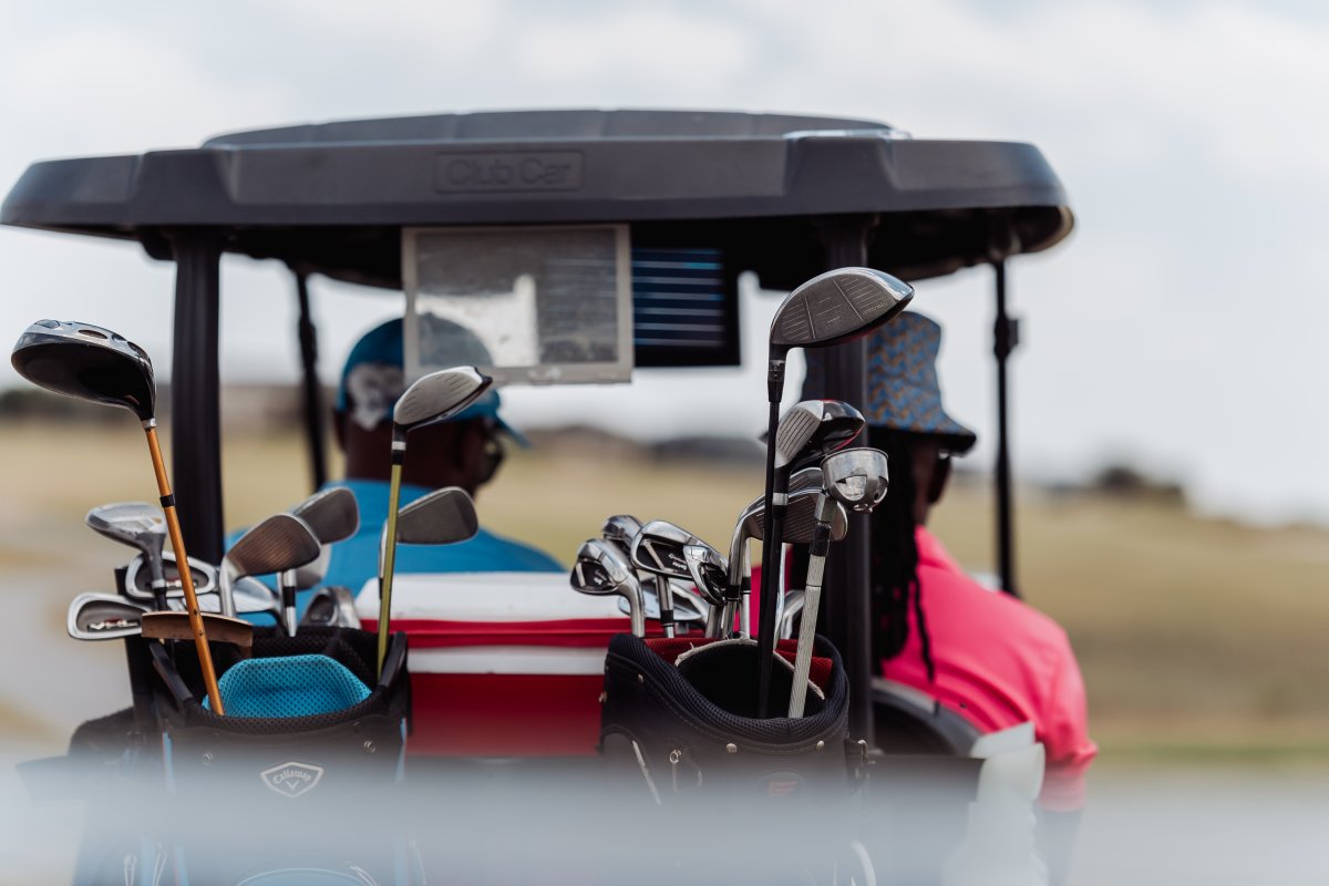 Golf clubs in the back of a golf cart with two black male golfers