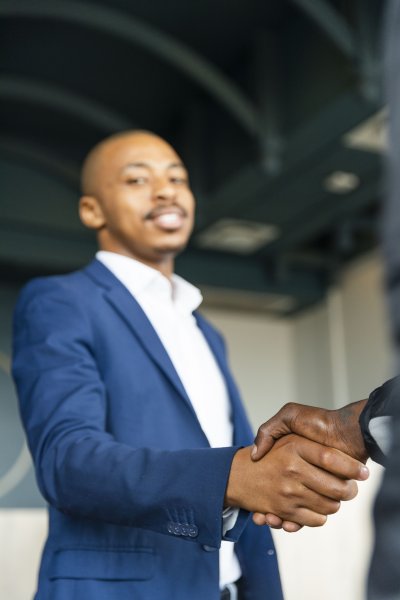Black business man hand shaking hands with a client at work and looking at the camera