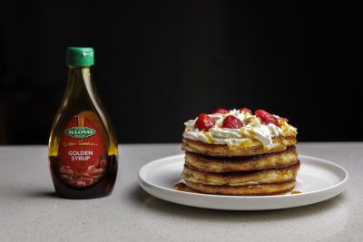 golden syrup bottle next to a plate of pancakes with strawberries and cream