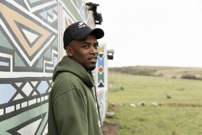 Black male posing next to a Ndebele painting