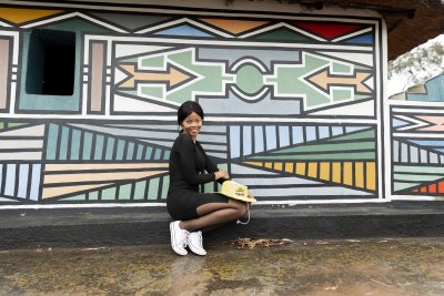 Black woman posing in front of Ndebele painting