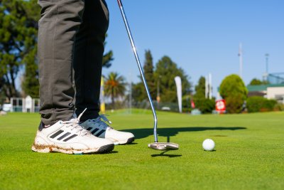 Black golfer wearing Adidas golf shoes putting on the green with a odyssey putter