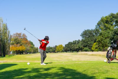 Black male golfer wearing a red golf shirt on the golf course hitting the ball