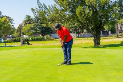 Black male golfer wearing a red golf shirt putting