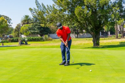 Black male golfer wearing a red golf shirt putting a golf ball