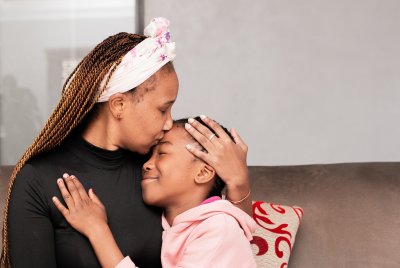 Black mother hugging daughter on the couch at home smiling.