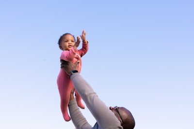 Black father holding daughter in the air with blue sky in the background in South Africa.