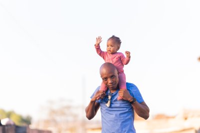 Black father carrying daughter on shoulders outside having fun wearing a blue shirt and watch.