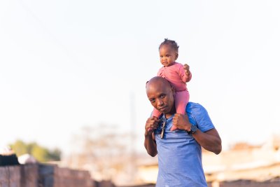 Father and daughter play outside, daughter wearing pink and father wearing a blue shirt on a sunny day.