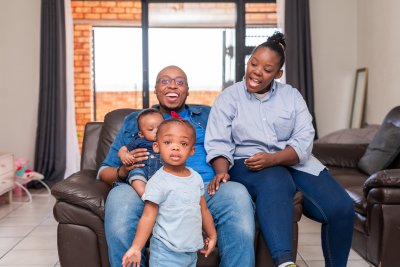 Toddler looking at camera in front of family at home on the couch.