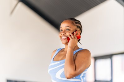 Black businesswoman talking on mobile phone smiling at the office with a blue top and braids.