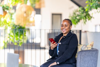 Black corporate woman sitting on the couch in a co working space holding phone.