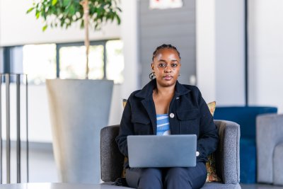 Professional black woman working on laptop at the office wearing a black jacket.