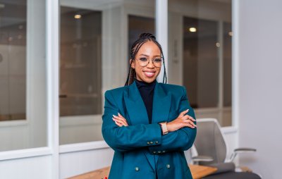 Young African business woman smiling at the office wearing a green jacket and glasses.