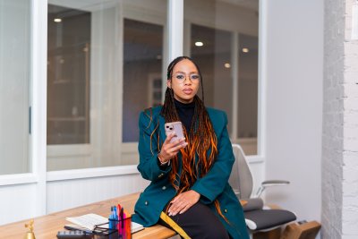 Professional young black woman holding a phone at the office sitting on her desk.