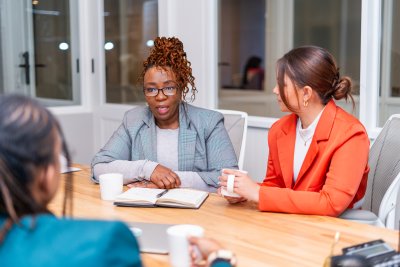 African mature black woman sitting at desk wearing glasses speaking to a candidate at an interview at the office for a job