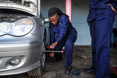 A young african women in blue overalls working on cars